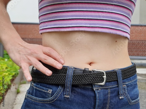 A young woman wears cropped clothing. She shows her belly button proudly and sexy and has her hand bent.