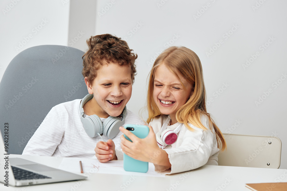Happy Caucasian Boy and Girl Learning Online with Laptops at Home, Sitting at a Table in the Living Room They are Wearing Headphones and Concentrating on their Studies, Connected to the Internet The
