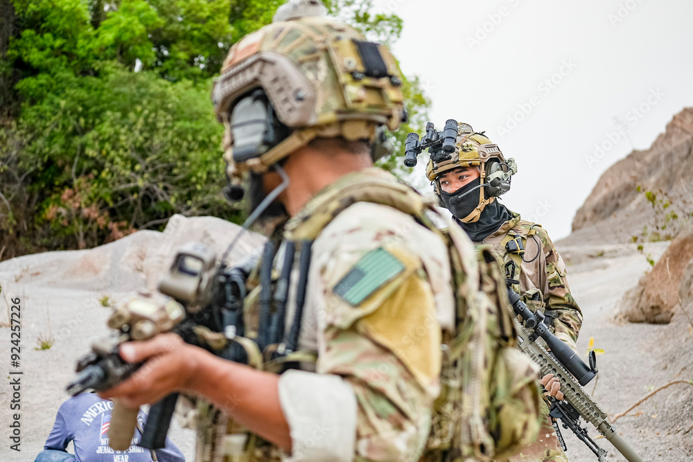 Obraz premium A group of military men in combat gear patrol in the middle of a desert and tropical jungle. Soldiers in full combat gear in dry weather conditions assemble and march on a mission.