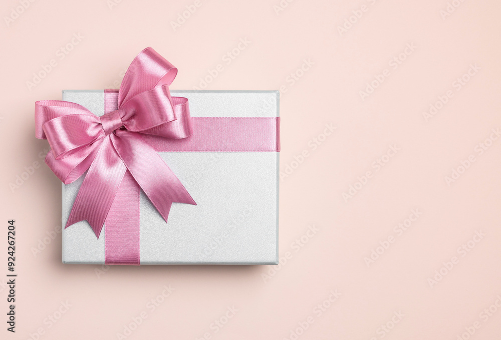 Beautiful gift box with pink bow on beige background, top view. Space for text Beautiful gift box with pink bow on beige background, top view. Space for text
