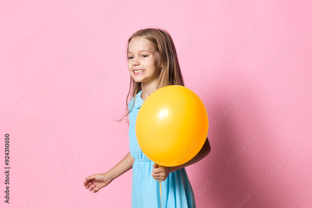 Joyful little girl in a blue dress holding a yellow balloon against a vibrant pink background Joyful little girl in a blue dress holding a yellow balloon against a vibrant pink background