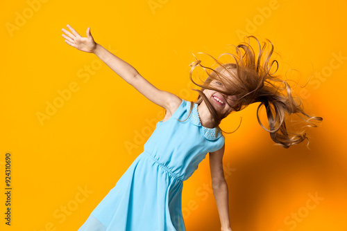 Joyful little girl in blue dress midjump against vibrant orange backdrop, capturing pure happiness and energy photo