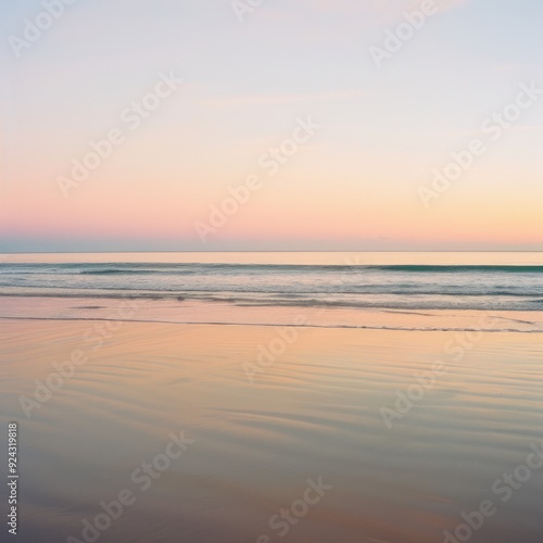 Tranquil beach at sunset with soft pink sky and calm waves.