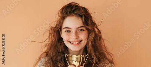 A cheerful young woman in stylish attire beams as she holds a contemporary vintage trophy, her smile and relaxed demeanor showcasing success. photo