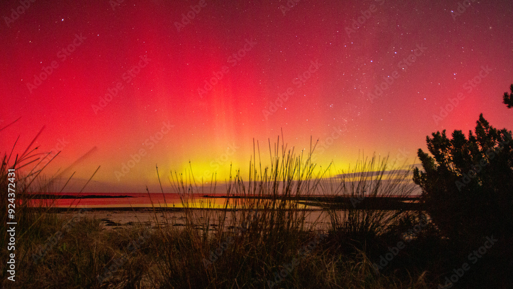 Φωτογραφία Colorful aurora australis lights up sky over beach.