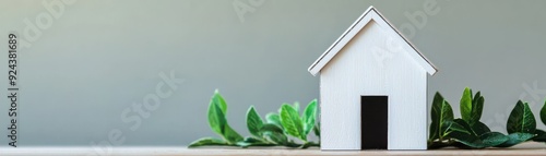 A minimalistic white house model surrounded by green leaves, symbolizing home, nature, and tranquility in a serene setting.