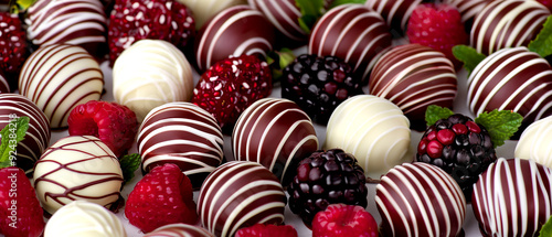 A close up of a variety of chocolate covered berries and raspberries. The chocolate is white and brown and the berries are red. Concept of indulgence and luxury, as the combination of chocolate