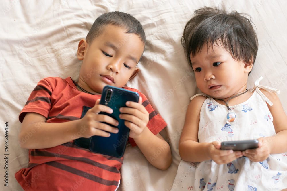 Boys and girls, brothers and sisters, sleep in the bed at home watching mobile phones. The concept of love, the warmth of the family. Boys and girls, brothers and sisters, sleep in the bed at home watching mobile phones. The concept of love, the warmth of the family.