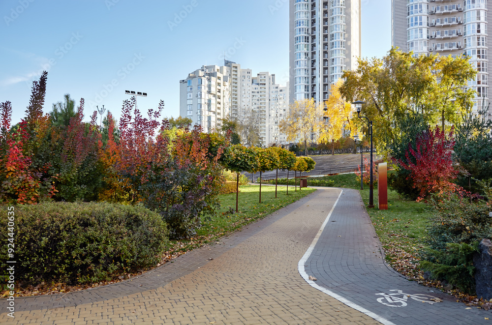 Fototapeta premium Walkway surrounded by trees and lawns in Kyiv, Europe. Recreation place in the autumn city park