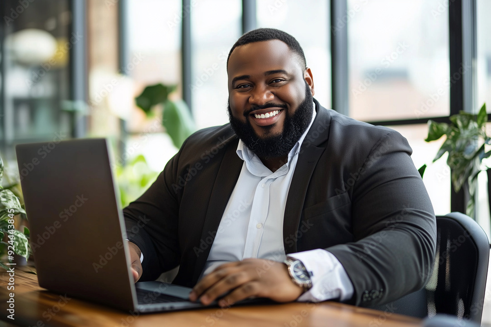 Plus size man with a big smile on his face is sitting at a desk with a laptop 