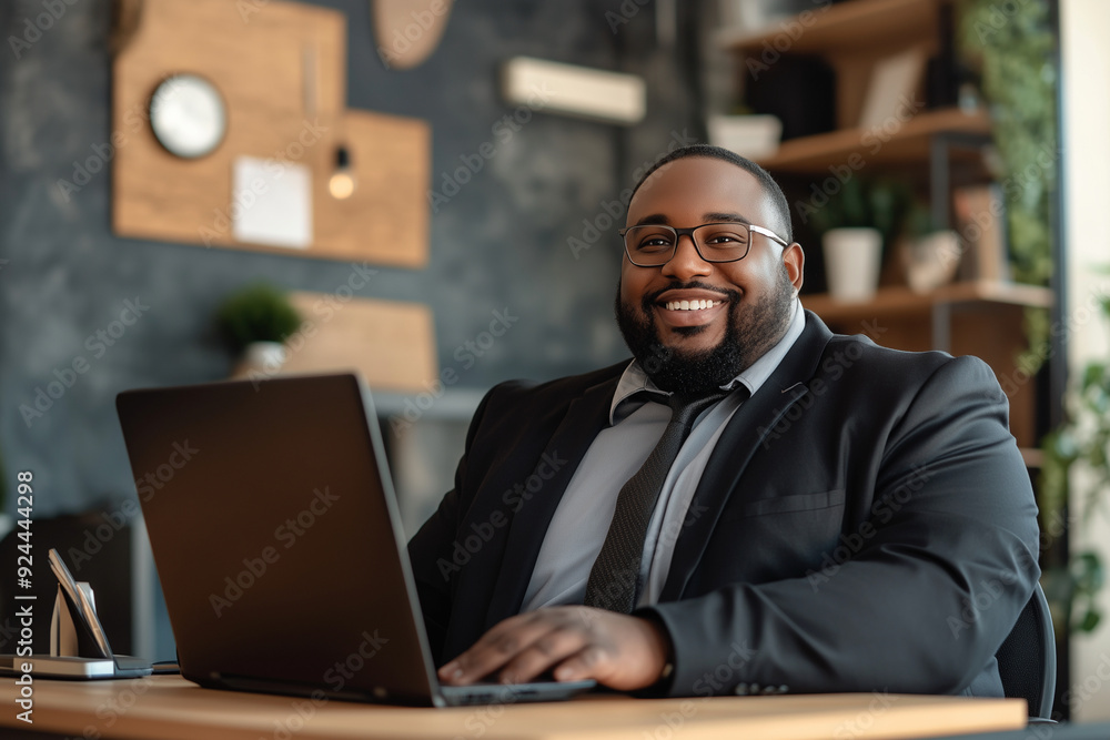 Plus size man with a big smile on his face is sitting at a desk with a laptop Plus size man with a big smile on his face is sitting at a desk with a laptop