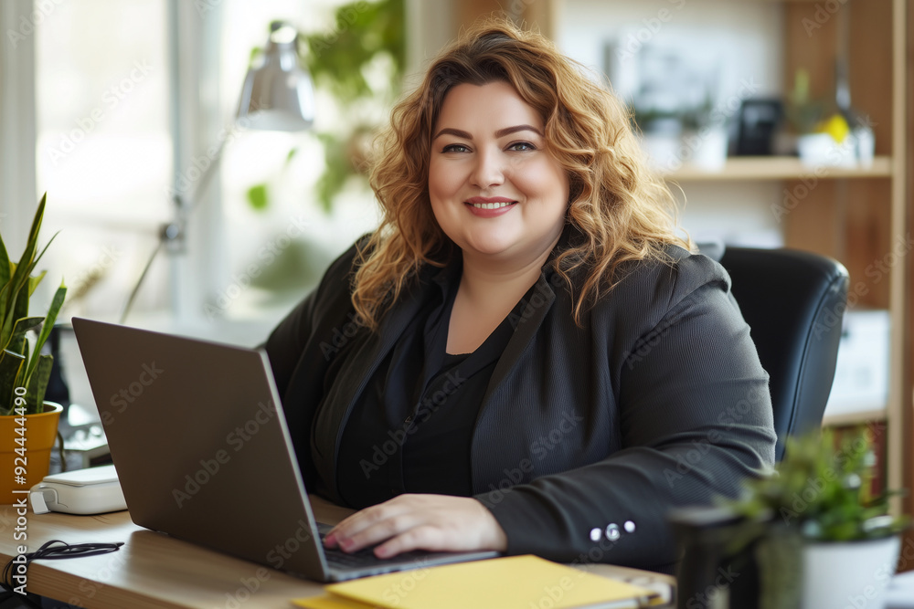 Plus size woman with a big smile on her face is sitting at a desk with a laptop Plus size woman with a big smile on her face is sitting at a desk with a laptop