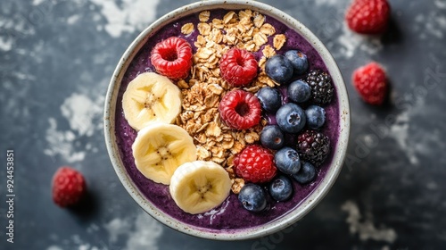 Top view of a bowl of acai topped with granola, banana slices, and fresh berries. Bright and colorful presentation.