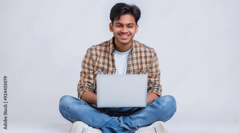 a happy young Indian man using a laptop, sitting on the floor with his legs crossed on an isolated white background a happy young Indian man using a laptop, sitting on the floor with his legs crossed on an isolated white background