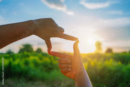 Two hands forming a diamond shape, with one hand pointing towards the sun
