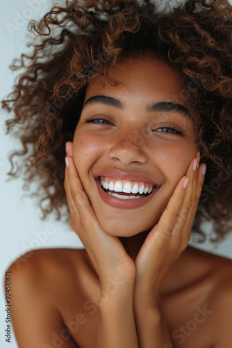 A beautiful African American woman, with curly hair, smiling and holding her hands on her face in a joyful expression photo