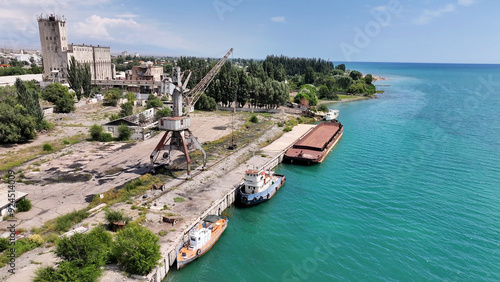 View of the abandoned sea port in Central Asia. Drone view on maritime city and port with old crane, barge and tug. Vivid Issyk-Kul scenery. photo