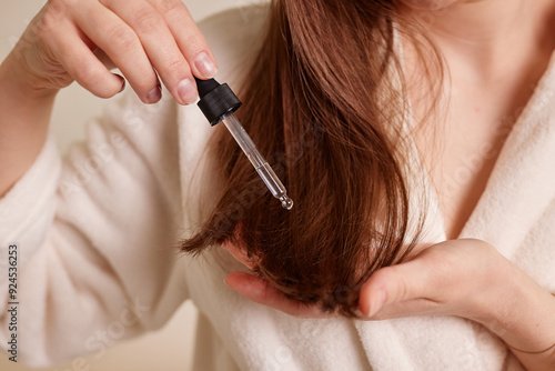 Cuadro en lienzo A young woman applies a drop of oil from a pipette to her hair, close-up