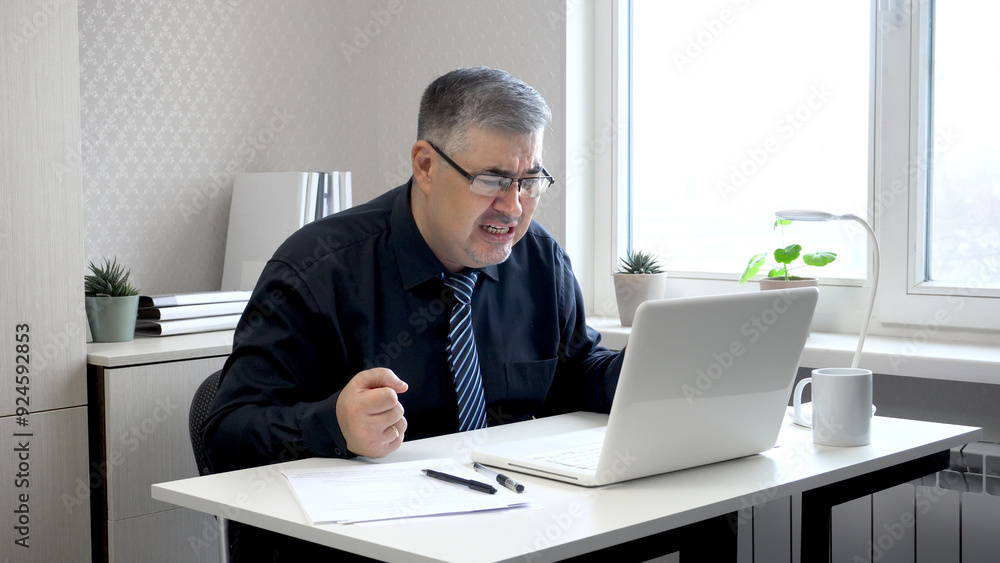 A man working at a computer in despair. He clenches his fists and looks at the monitor screen with anger. A man working at a computer in despair. He clenches his fists and looks at the monitor screen with anger.