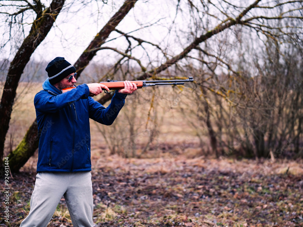 A man in a blue jacket is holding a shotgun. The image has a mood of excitement and anticipation, as the man is preparing to shoot a target. Sport and hobby concept. Male with a rifle. A man in a blue jacket is holding a shotgun. The image has a mood of excitement and anticipation, as the man is preparing to shoot a target. Sport and hobby concept. Male with a rifle.