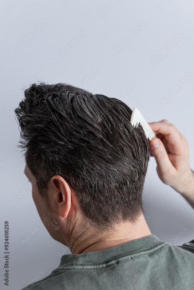 Side view from the back of the head of a man combing his gray hair with a comb. Copy space. Isolated on gray background. Hair styling and hair care concept Side view from the back of the head of a man combing his gray hair with a comb. Copy space. Isolated on gray background. Hair styling and hair care concept