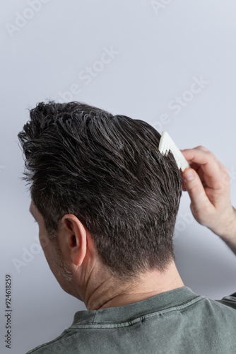 Side view from the back of the head of a man combing his gray hair with a comb. Copy space. Isolated on gray background. Hair styling and hair care concept