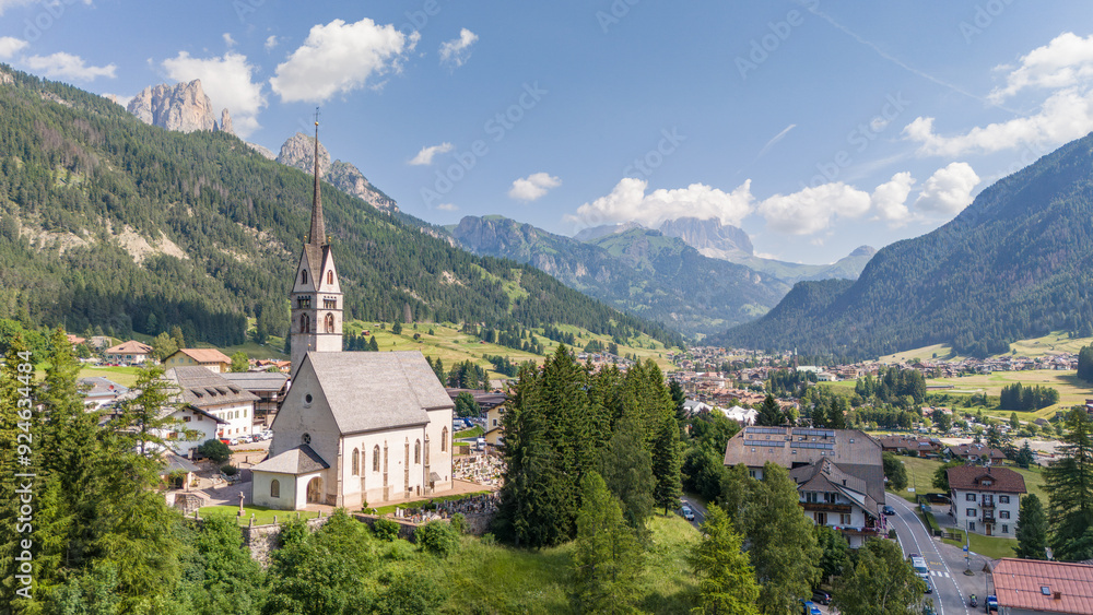 Aerial drone view of church of S. Giovanni in Vigo di fassa, Val di fassa valley, Trentino, a town in the Italian dolomites. Church and houses, sunny summer day. Mountain landscape. Dolomites. Aerial drone view of church of S. Giovanni in Vigo di fassa, Val di fassa valley, Trentino, a town in the Italian dolomites. Church and houses, sunny summer day. Mountain landscape. Dolomites.