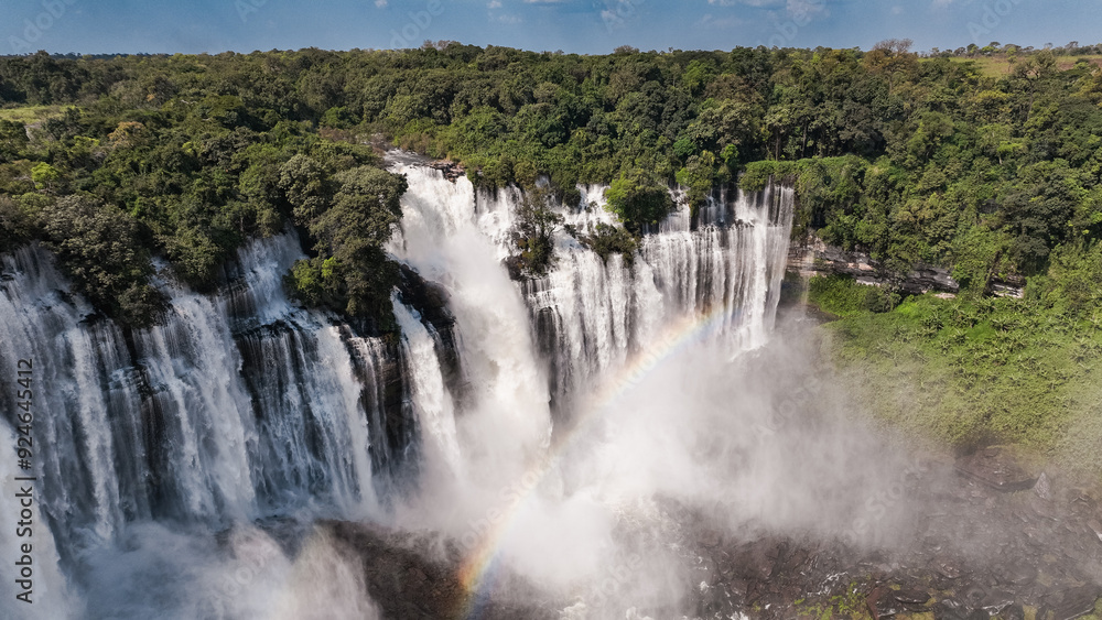 Fototapeta premium Kalandula Waterfall cascades in Angola with vibrant rainbow above lush greenery during daylight