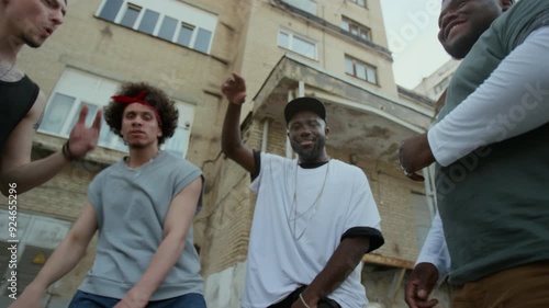 Low angle view of gritty male musician holding handgun and rapping on camera expressively with hip hop group standing in city street photo