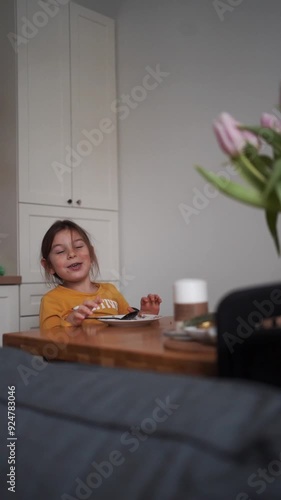 Young girl in a yellow sweater enjoying a meal at a table in a cozy home kitchen.