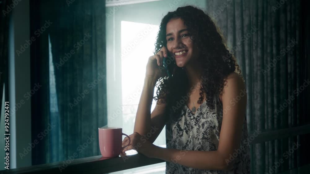 A happy, attractive curly-haired African female or woman, smiling while chatting or talking on a mobile phone, a cup of coffee at her side. concept of holiday, relaxed weekend mornings A happy, attractive curly-haired African female or woman, smiling while chatting or talking on a mobile phone, a cup of coffee at her side. concept of holiday, relaxed weekend mornings