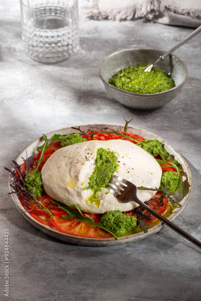 Tomato salad with burrata cheese and green pesto on gray background. Tomato salad with burrata cheese and green pesto on gray background.