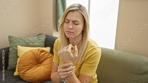 Fotografía Young caucasian woman in pain holding wrist in a modern living room interior