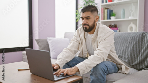 Man using laptop in a well-lit modern living room, showcasing everyday technology at home.