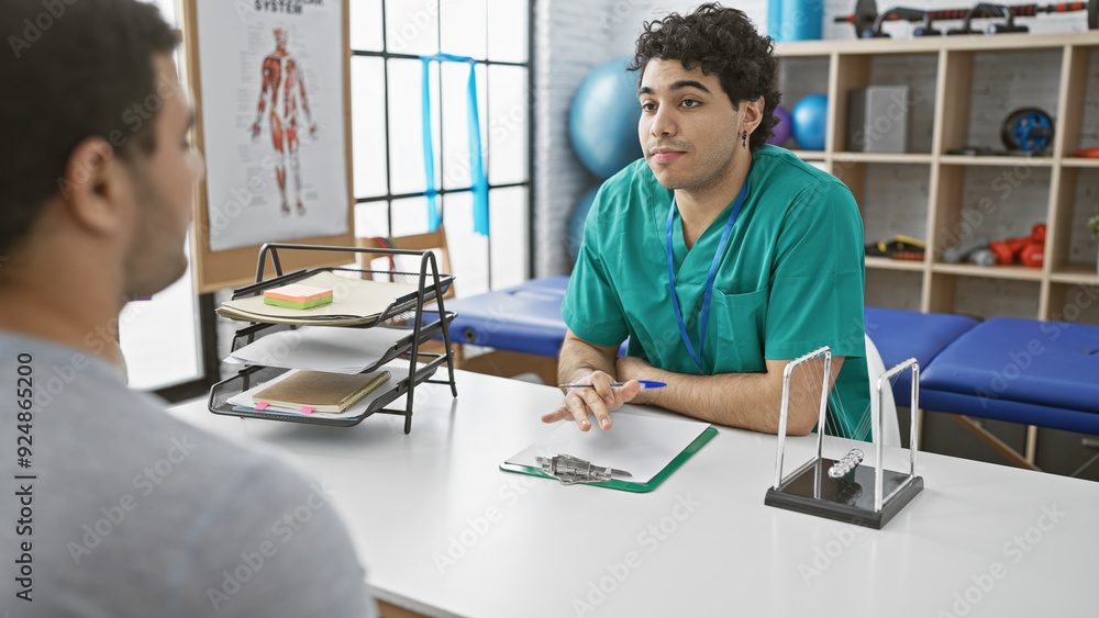 Obraz premium In a well-equipped physiotherapy clinic, a male therapist consults with a patient, symbolizing healthcare and rehabilitation indoors.