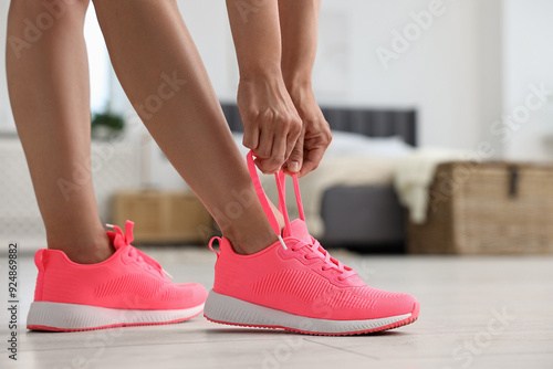 Woman tying shoelace of pink sneaker indoors, closeup. Space for text