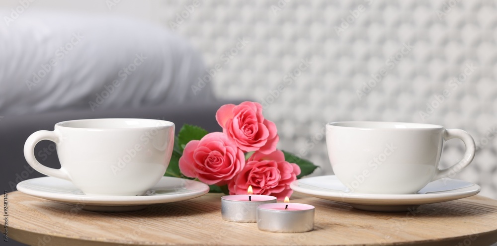 Burning candles, two cups of drink and flowers on coffee table indoors, closeup Burning candles, two cups of drink and flowers on coffee table indoors, closeup