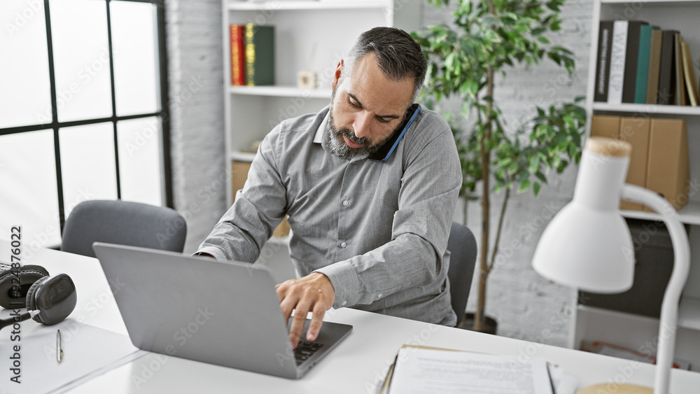Senior hispanic man with beard and grey hair multitasking in a modern office. Senior hispanic man with beard and grey hair multitasking in a modern office.