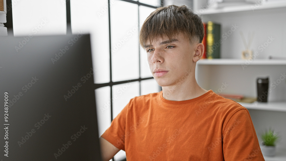 A focused young man studying on a computer at a modern home office setup. A focused young man studying on a computer at a modern home office setup.
