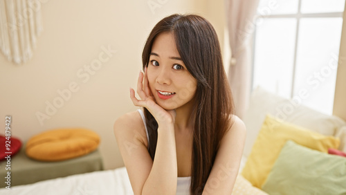 A portrait of a smiling young asian woman sitting comfortably in a cozy, well-lit bedroom photo