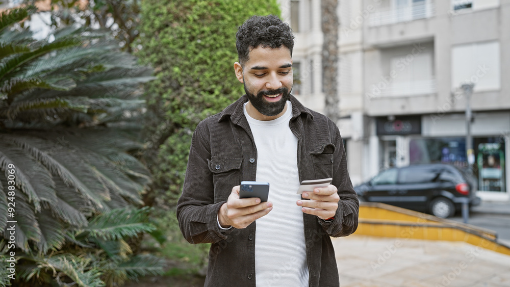 Fototapeta premium Handsome young adult hispanic man with beard holding credit card and smartphone on city street.