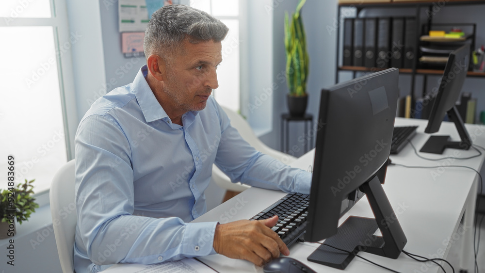 Man working at a computer in a modern office setting featuring indoor plants and organized shelves in the background Man working at a computer in a modern office setting featuring indoor plants and organized shelves in the background