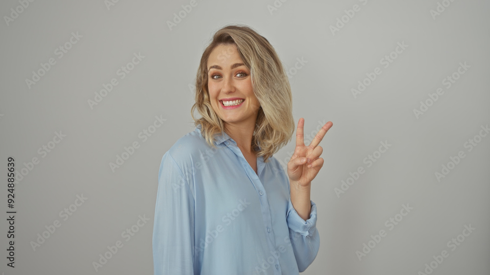 A cheerful blonde woman in a blue shirt making a peace sign against a white background. A cheerful blonde woman in a blue shirt making a peace sign against a white background.