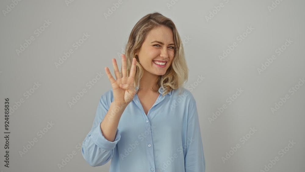 A smiling blonde woman gestures four against a white background, symbolizing counting or selection in casual attire. A smiling blonde woman gestures four against a white background, symbolizing counting or selection in casual attire.