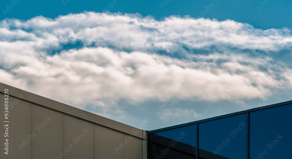 corner of a modern building with a window and a blue sky with clouds