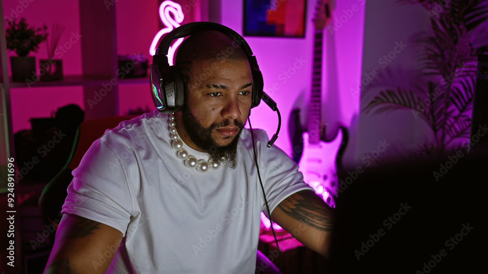 Fototapeta premium Handsome bearded man with headphones in a neon-lit gaming room at night, concentrating on gaming.