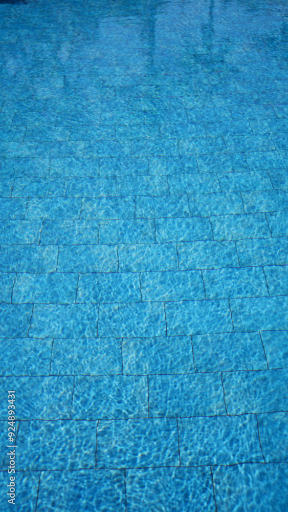 Close-up of sunlight reflecting on the serene, blue, rippling water of a tiled swimming pool. Close-up of sunlight reflecting on the serene, blue, rippling water of a tiled swimming pool.