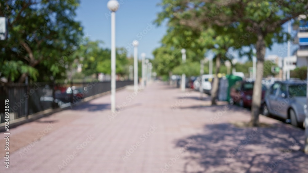Blurred outdoor sidewalk scene featuring trees, cars, and streetlights on a sunny day, creating a defocused summer atmosphere in a bustling urban area Blurred outdoor sidewalk scene featuring trees, cars, and streetlights on a sunny day, creating a defocused summer atmosphere in a bustling urban area