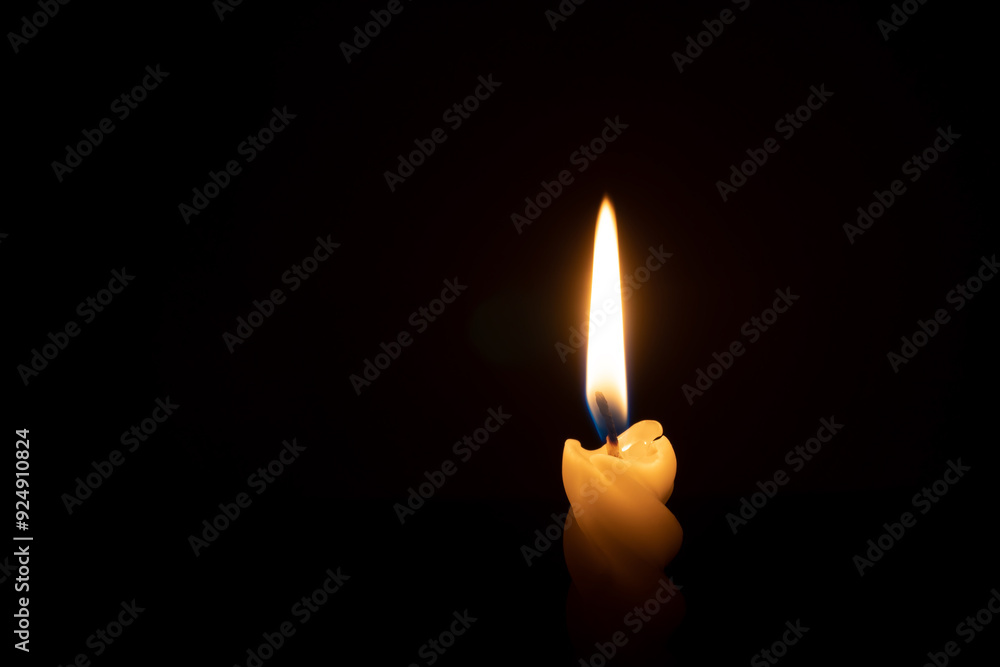 A single burning candle flame or light glowing on a spiral white candle on black or dark background on table in church for Christmas, funeral or memorial service with copy space A single burning candle flame or light glowing on a spiral white candle on black or dark background on table in church for Christmas, funeral or memorial service with copy space