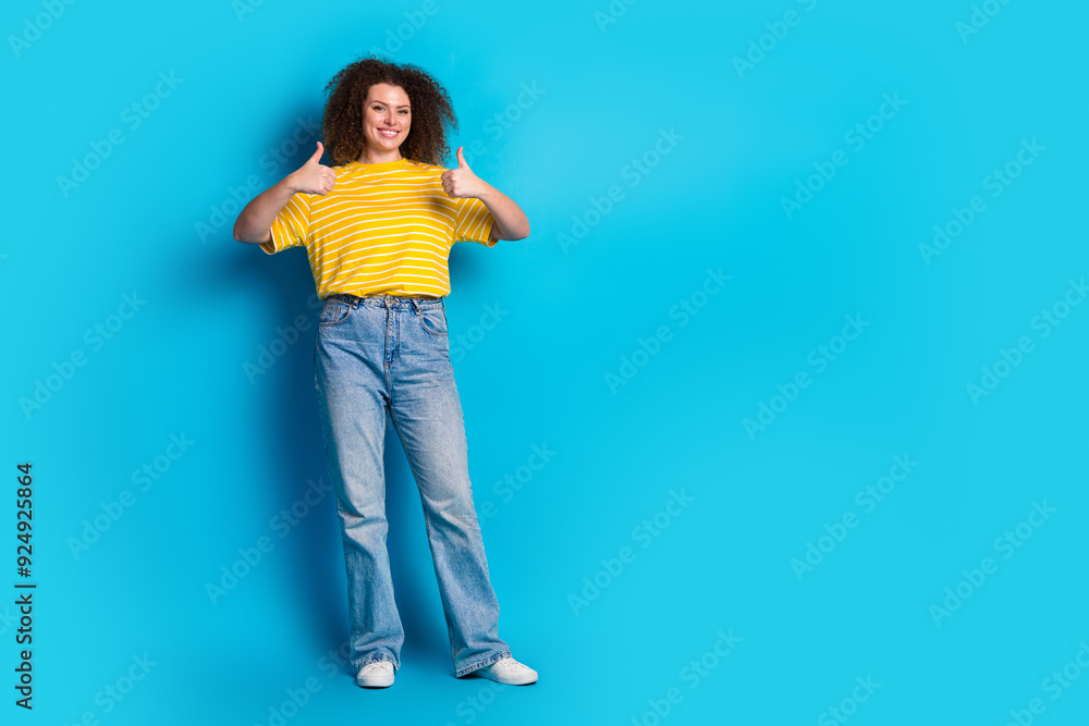 Full length photo of lovely young lady thumb up approve dressed stylish striped yellow garment isolated on blue color background Full length photo of lovely young lady thumb up approve dressed stylish striped yellow garment isolated on blue color background